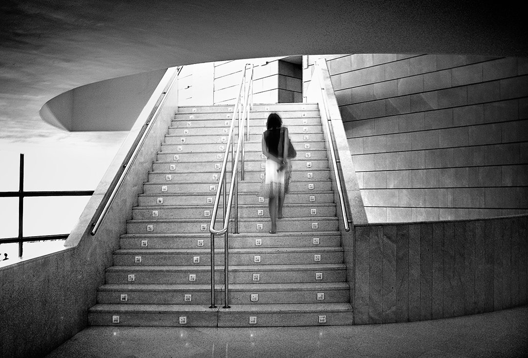 Una persona sube una escalera entre muros y planos curvos.